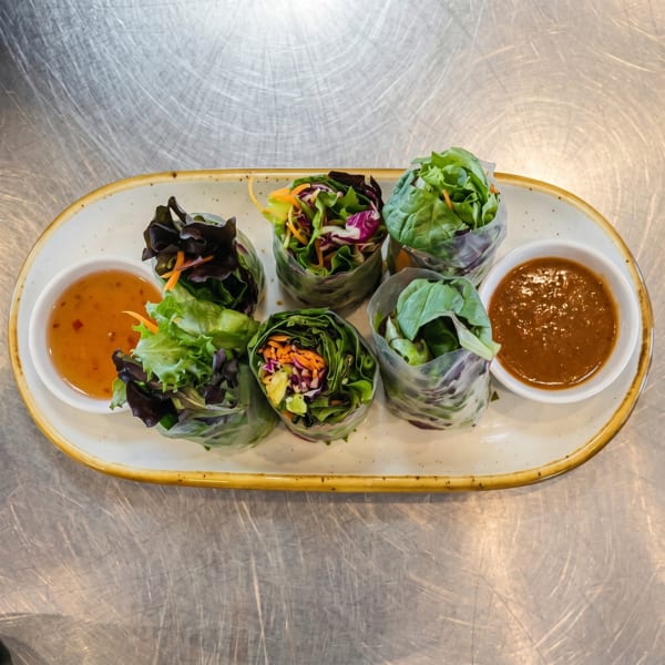 Six fresh spring rolls filled with vibrant greens and shredded vegetables, served with two dipping sauces.