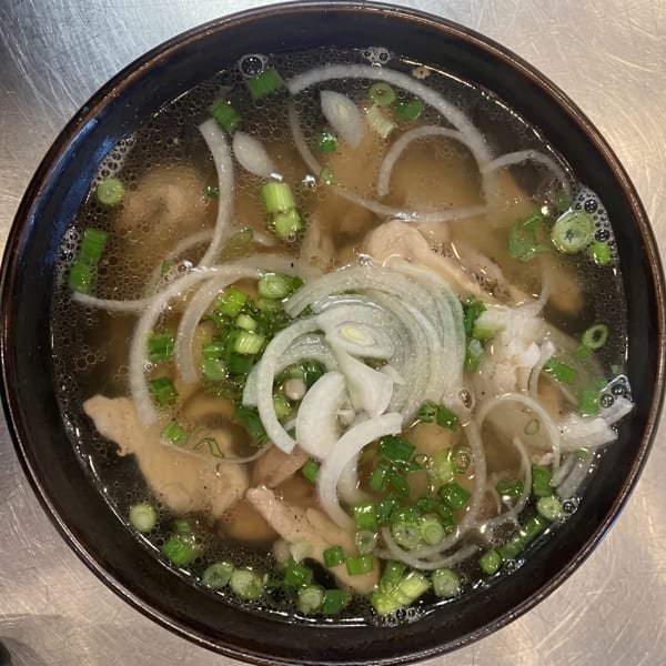 Close-up of a bowl of pho with chicken, sliced onions, and green onions in a rich broth.