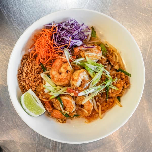 Shrimp Pad Thai with shredded carrots, red cabbage, peanuts, and a lime wedge in a white bowl.